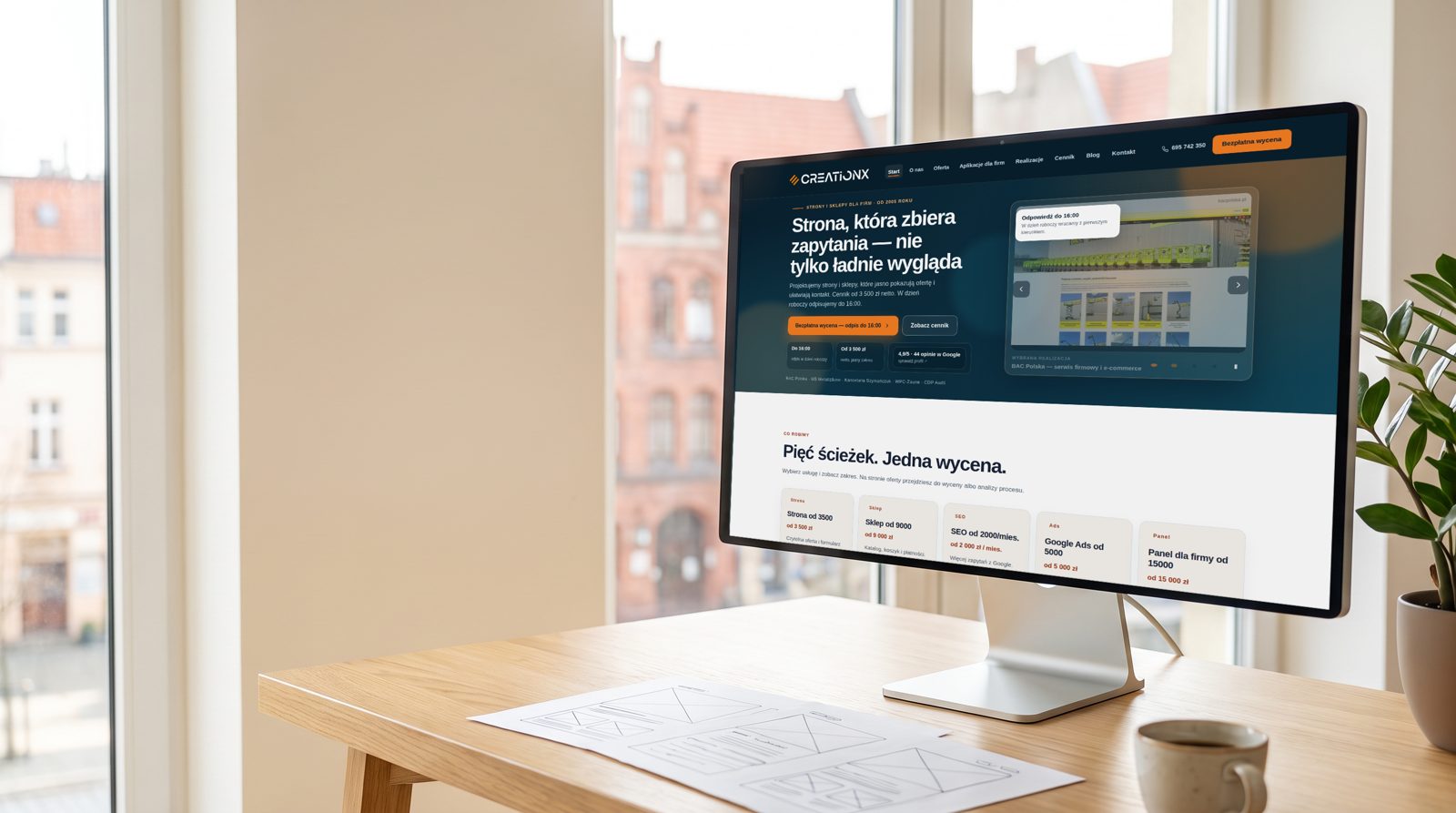 Monitor na dębowym biurku, na ekranie strona creationX